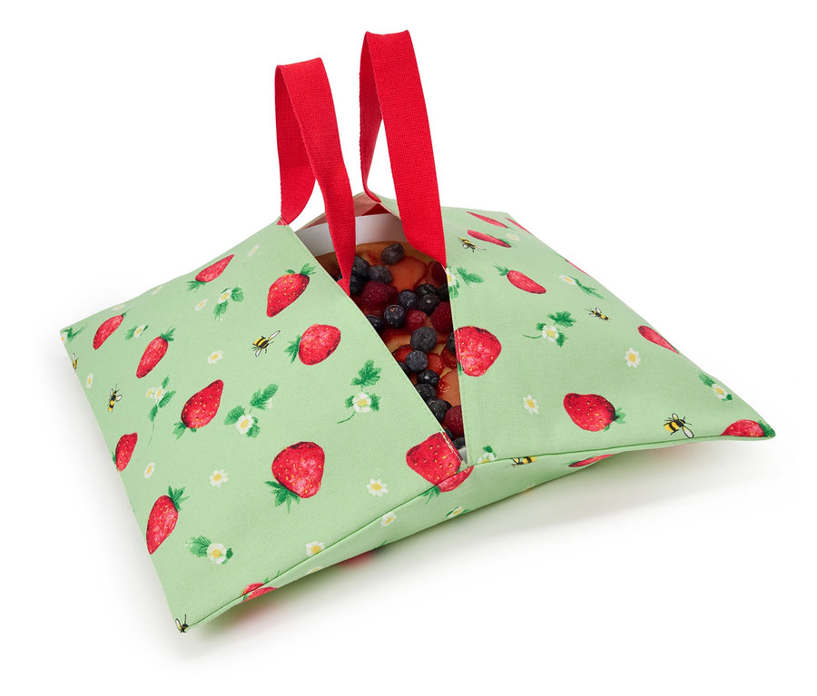 Tarte aux fraises dans un sac en tissu vert à motif de fraises avec des anses rouges.
