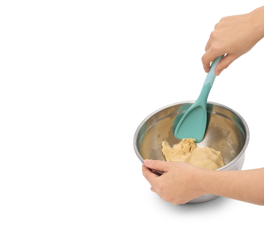 Une personne mélange de la pâte dans un bol en métal avec une spatule turquoise.