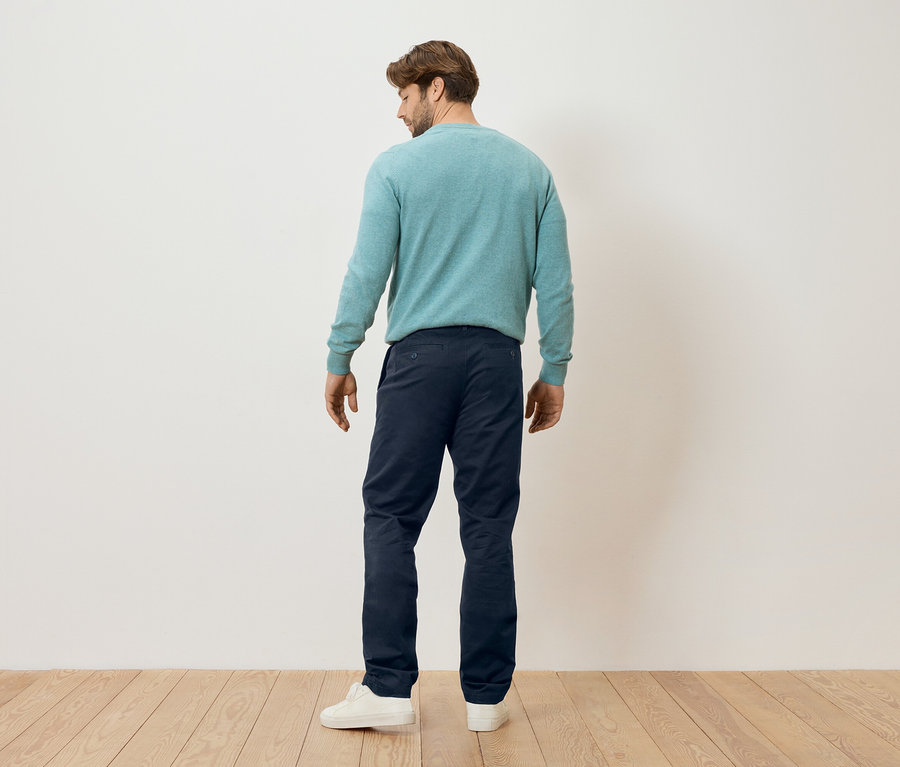 Un homme se tient dos à la caméra, il porte un pull couleur menthe, un pantalon bleu marine et des baskets blanches.