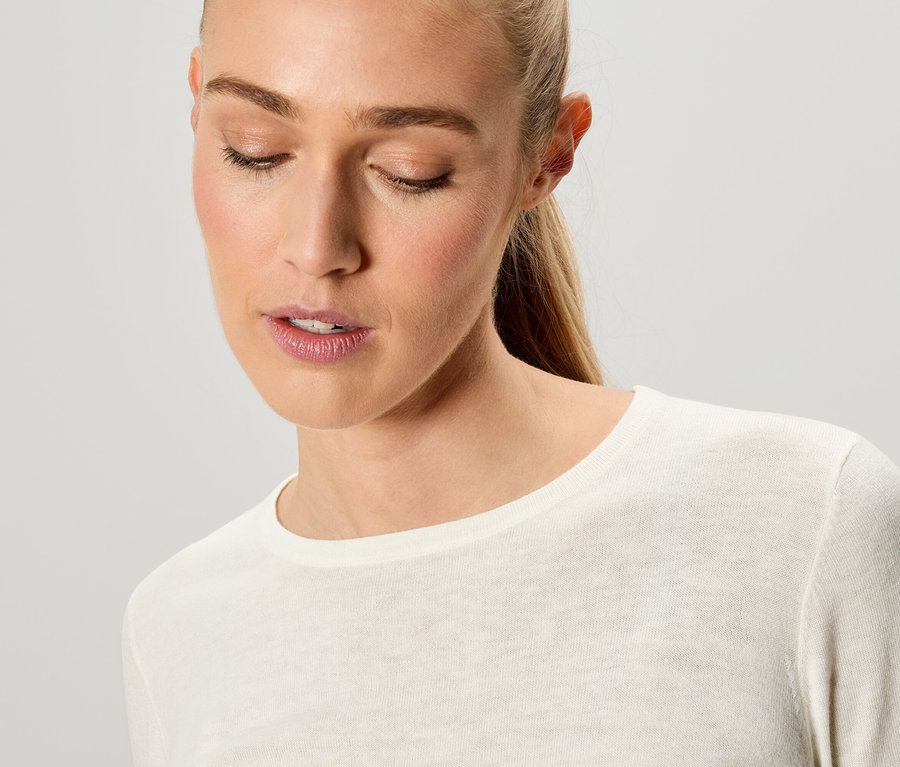 Portrait d'une femme blonde aux yeux clos portant un t-shirt crème à manches longues.