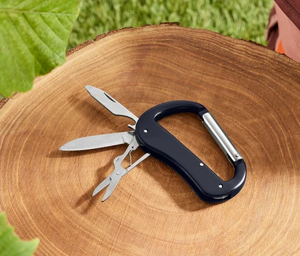 Un outil multifonction noir avec un mousqueton repose sur une souche d'arbre.