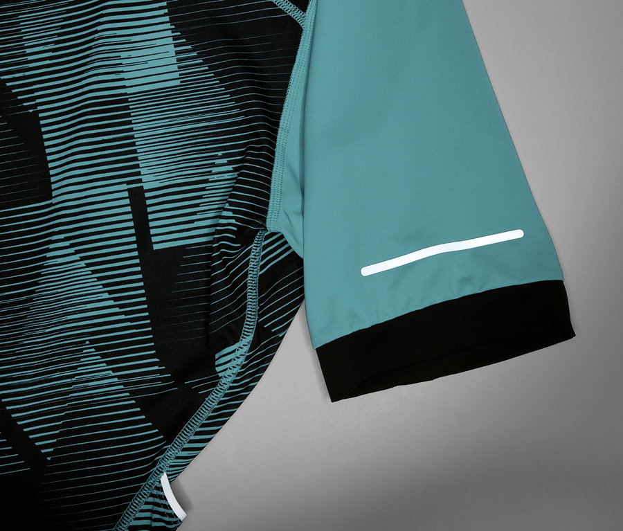 Gros plan d'un maillot de cyclisme avec une manche turquoise, un poignet noir et une bande réfléchissante.