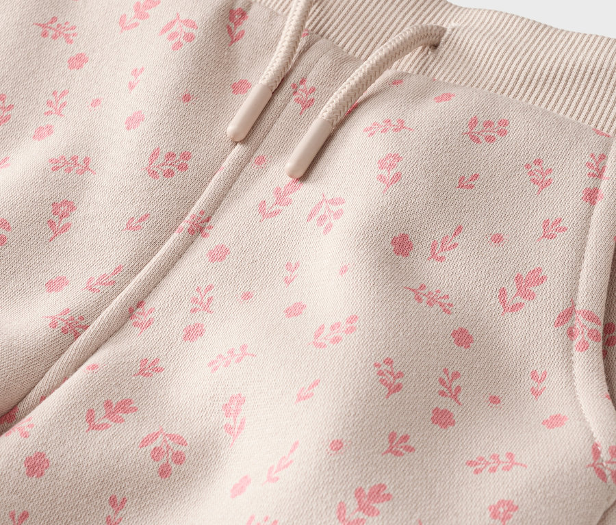 Gros plan d'un pantalon beige avec cordon de serrage et poche, recouvert d'un motif floral rose.
