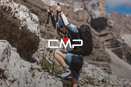 Une femme avec un sac à dos et des bâtons de randonnée escalade des rochers. Elle porte des chaussures de randonnée, un short et une veste.