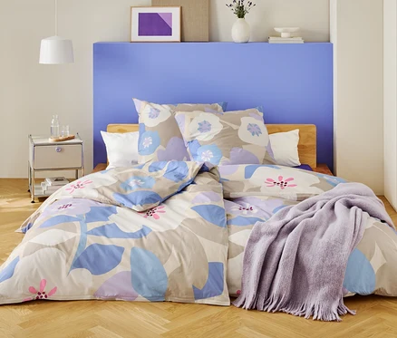 Une chambre avec un lit recouvert de draps à motifs floraux et d'une couverture violette.