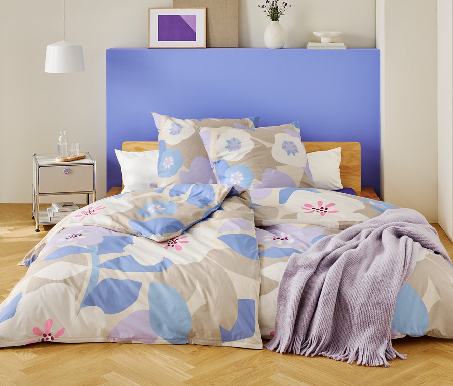 Une chambre avec un lit recouvert de draps à motifs floraux et d'une couverture violette.