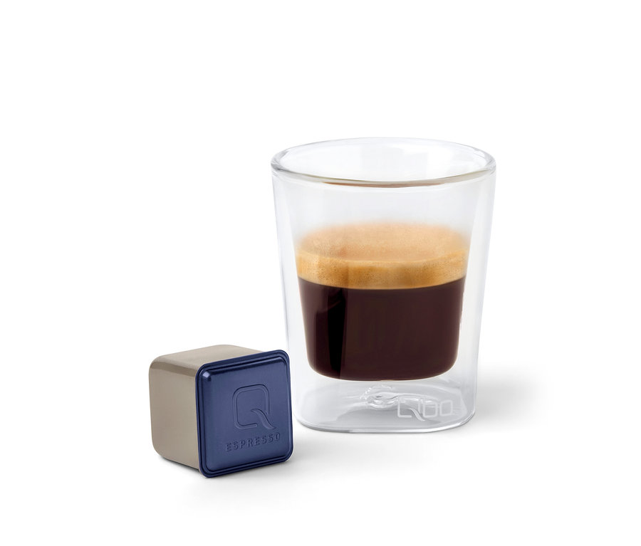 Une capsule de café Qbo Espresso INDIAN KAVERI à côté d'un verre d'espresso.