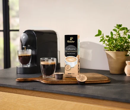 Machine à café versant du café dans un verre à côté d'un paquet de Cafissimo Decaffeinato – décaféiné – 10 capsules.