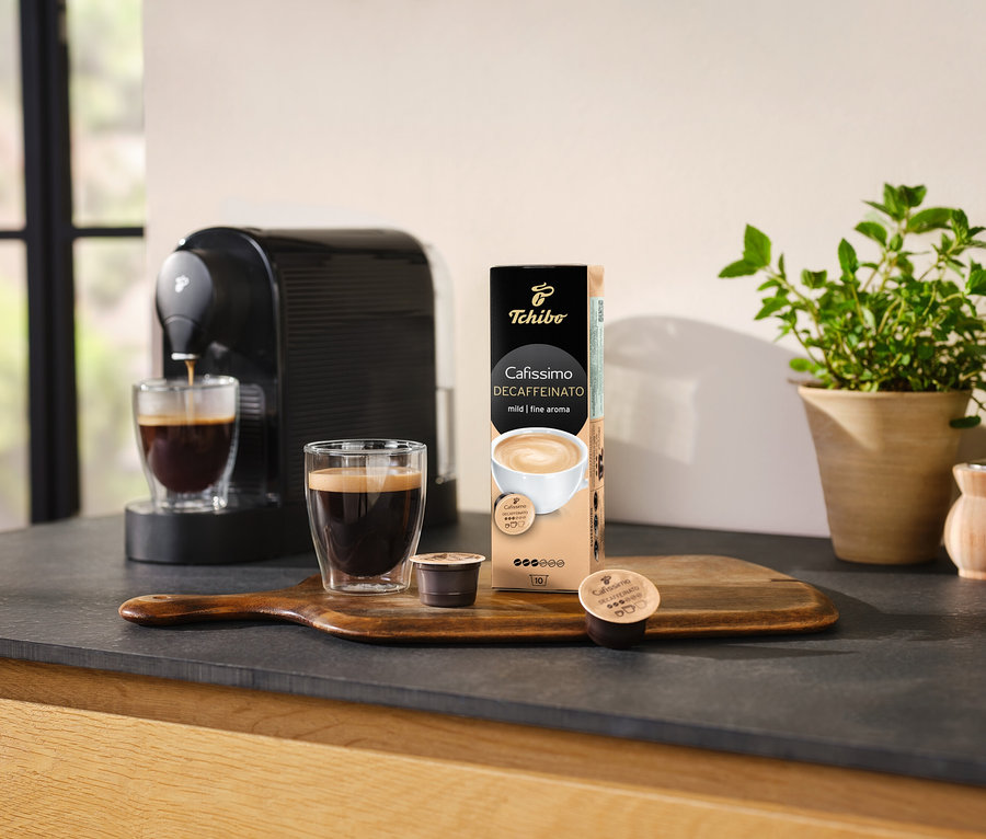Machine à café versant du café dans un verre à côté d'un paquet de Cafissimo Decaffeinato – décaféiné – 10 capsules.