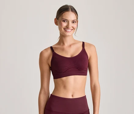 Femme souriante portant un soutien-gorge de sport bordeaux et un legging assorti, regardant l'appareil photo.