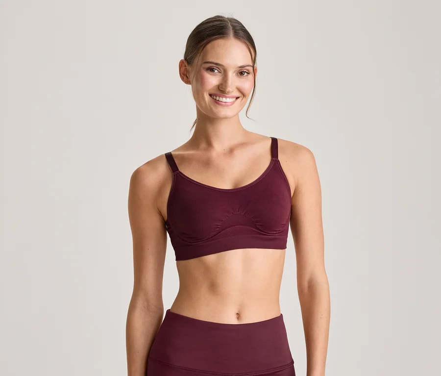 Femme souriante portant un soutien-gorge de sport bordeaux et un legging assorti, regardant l'appareil photo.