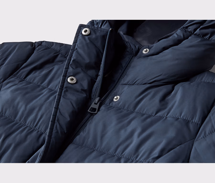 Gros plan d'une doudoune bleu marine. La veste présente une fermeture éclair partiellement ouverte, des boutons-pression argentés sur la patte et la capuche, ainsi qu'un design matelassé.