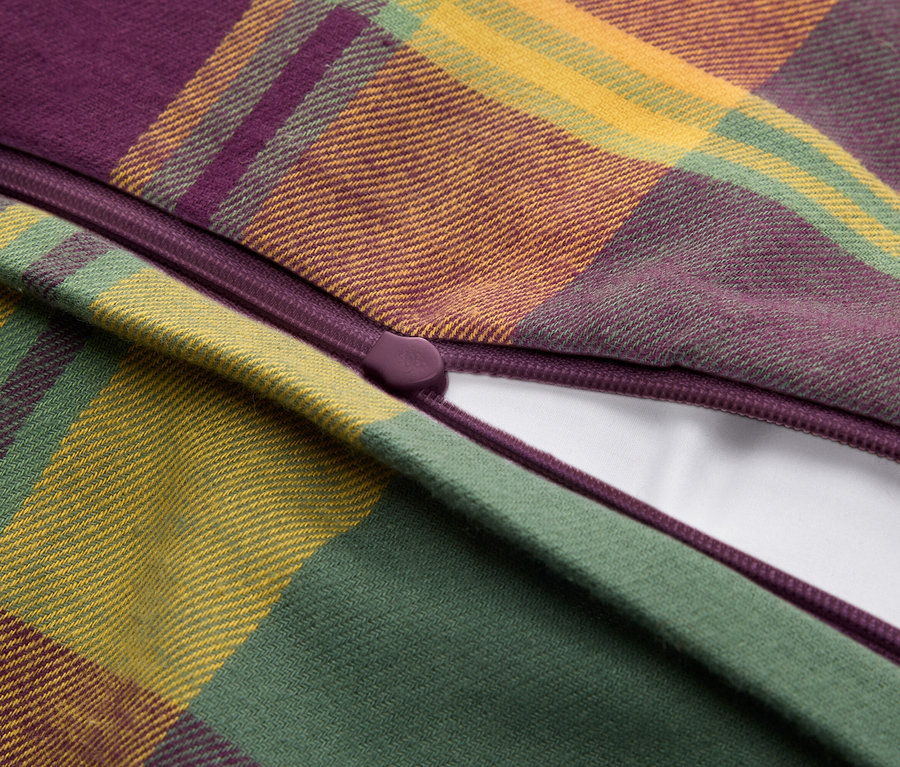 Gros plan d'un tissu écossais violet, vert et jaune, avec une fermeture éclair violette partiellement ouverte révélant un matériau blanc.