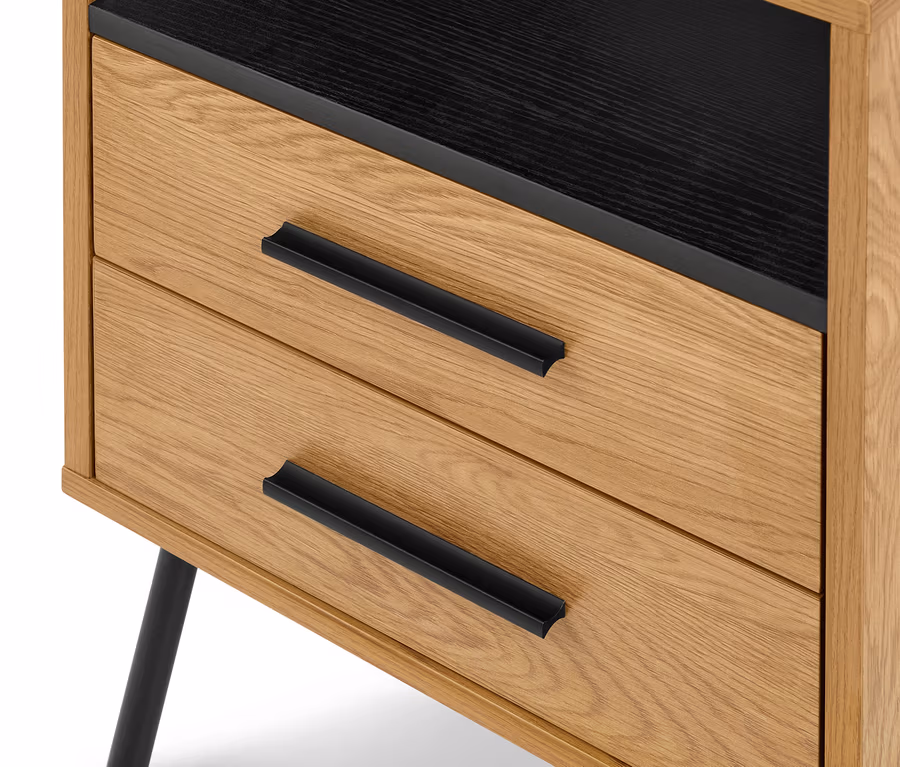 Gros plan d'une commode en bois clair avec deux tiroirs, chacun doté d'une longue poignée noire. La surface supérieure est noire et un pied noir est visible en bas à gauche.