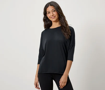 Une femme aux cheveux bruns pose dans un t-shirt noir à manches trois-quarts et un legging noir.