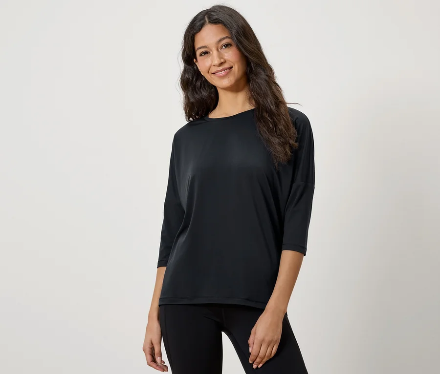 Une femme aux cheveux bruns pose dans un t-shirt noir à manches trois-quarts et un legging noir.