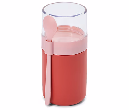 Un récipient alimentaire rouge avec une bande rose et un couvercle transparent, doté d'une cuillère rose attachée sur le côté.