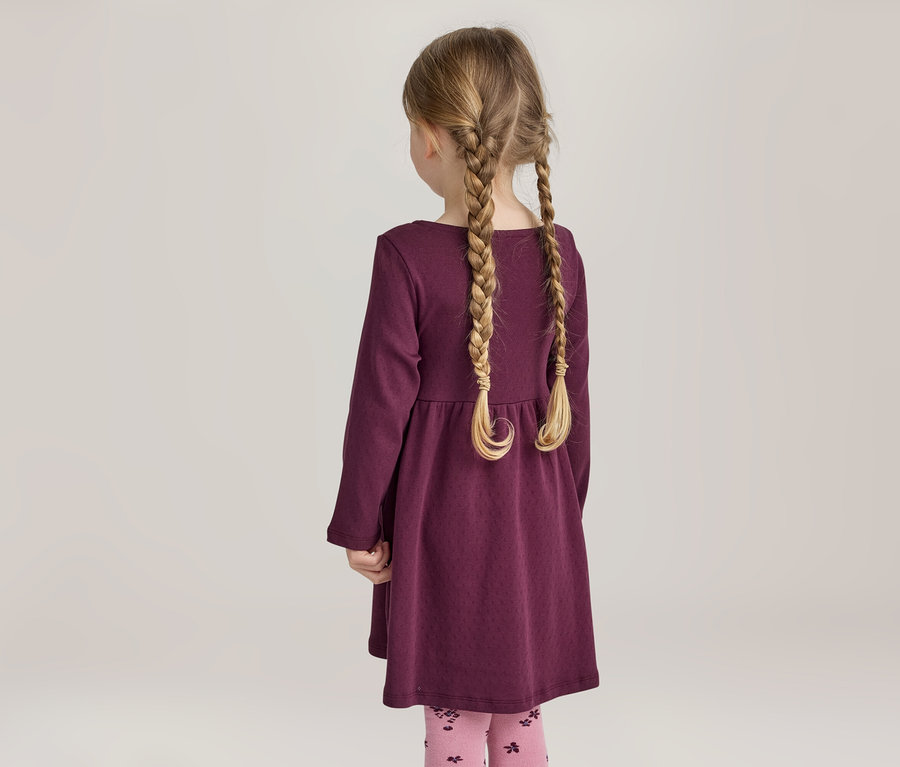 Fille vue de dos avec des tresses blondes, portant une robe violette et des leggings roses à motifs.