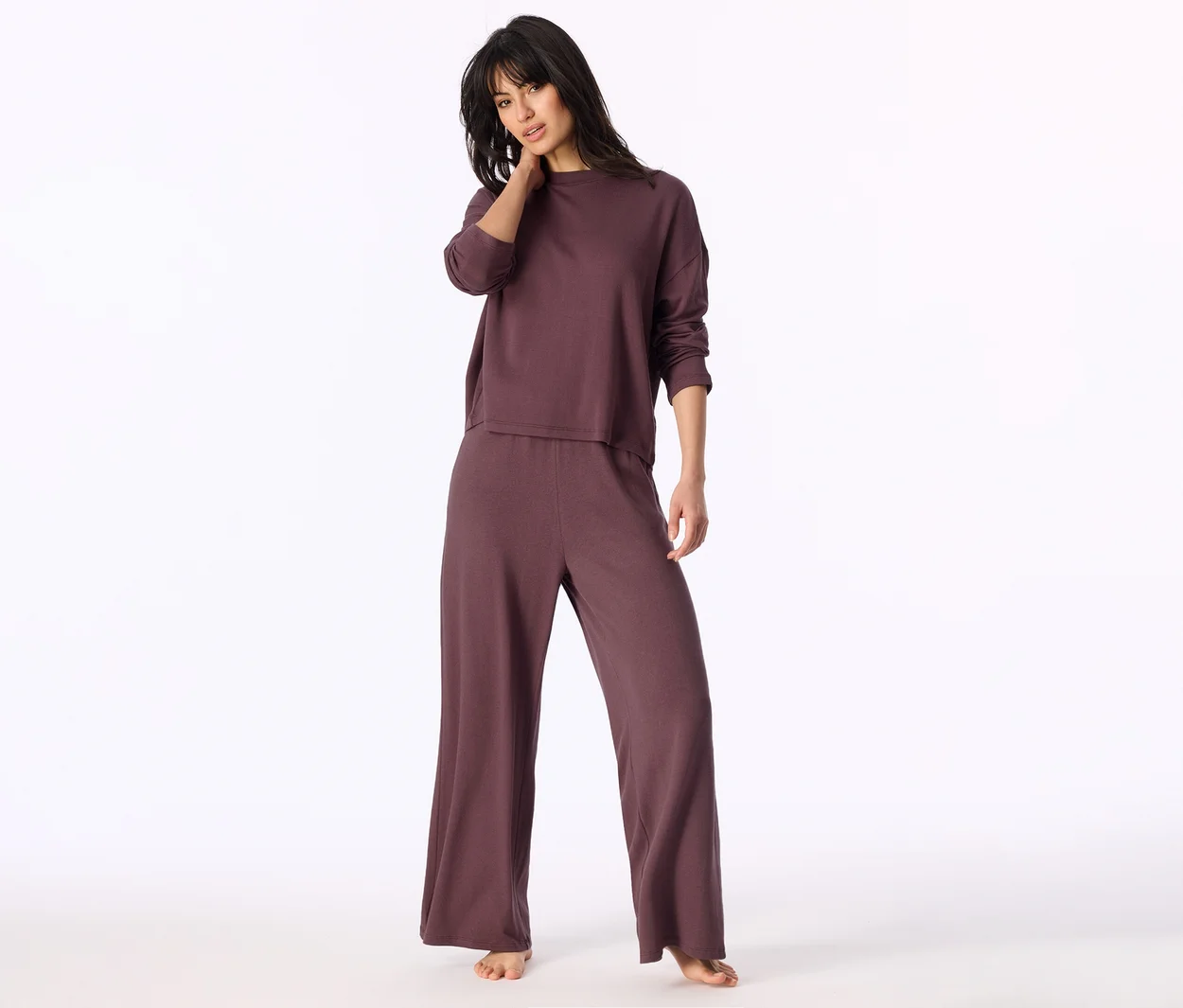 Femme debout portant un haut à manches longues prune foncé et un pantalon large assorti, une main sur le cou.