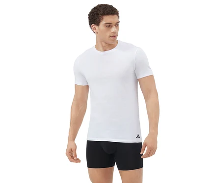 Homme debout, portant un t-shirt blanc à manches courtes et un boxer noir, regardant vers la droite sur un fond blanc.