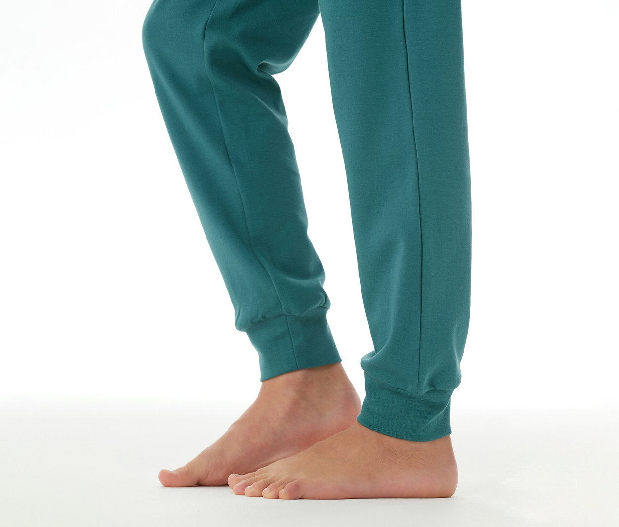 Jambes d'enfant portant un bas de pyjama couleur pétrole avec des chevilles élastiques, pieds nus.