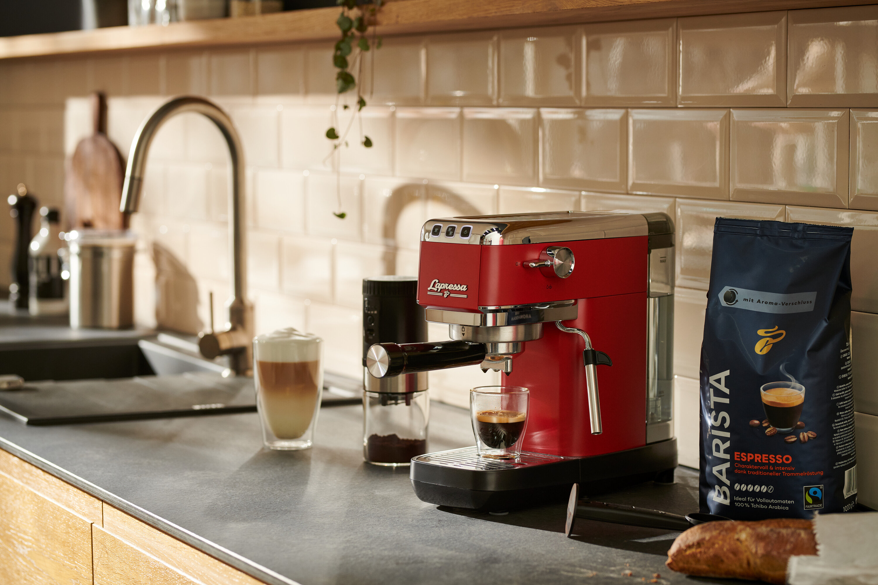 Une machine à porte-filtre rouge « Lapressa » prépare du café dans un verre. À côté se trouvent un moulin à café et un paquet de café.