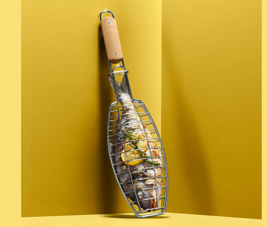 Un poisson dans une pelle à barbecue appuyée contre un mur jaune.