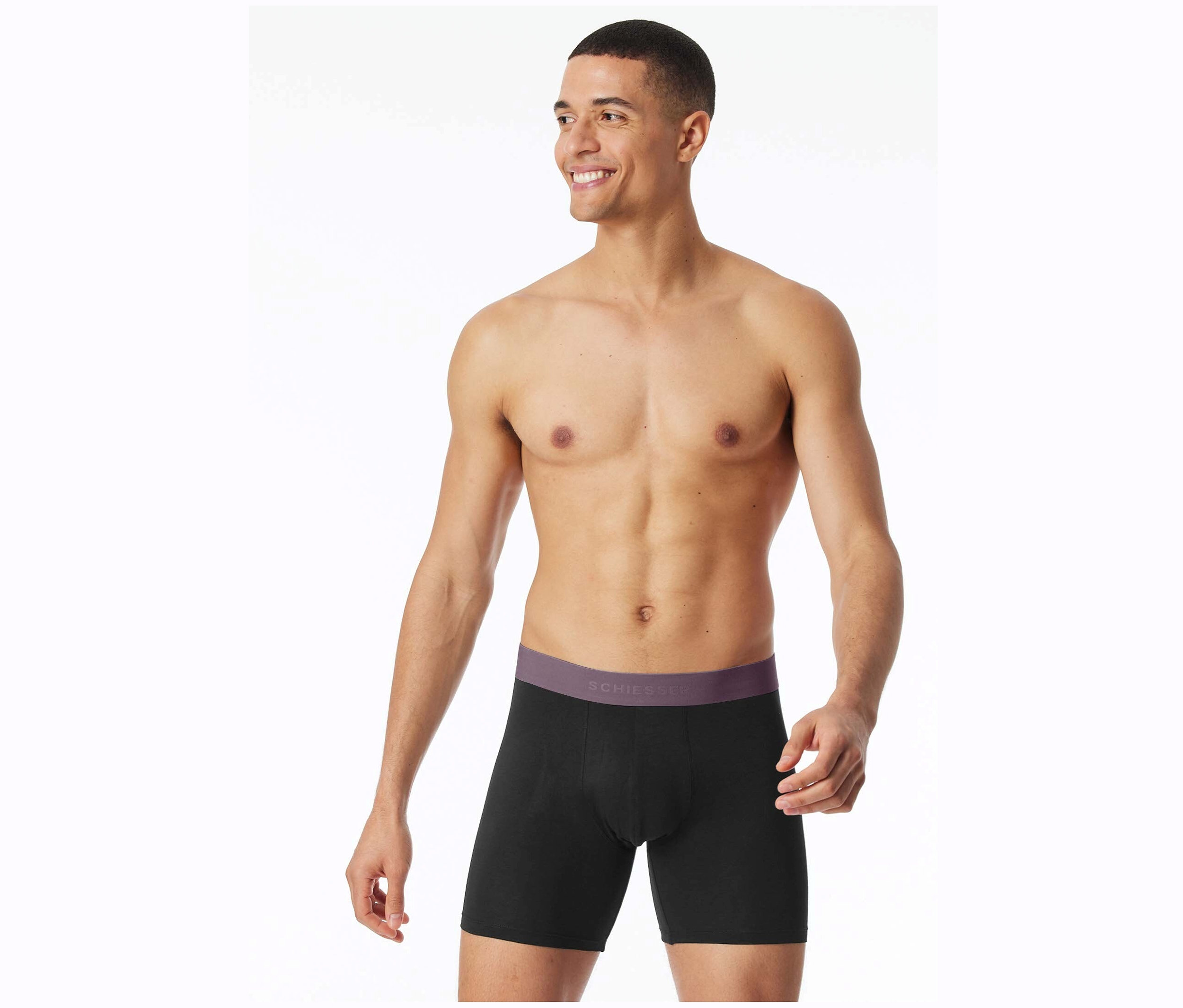 Un homme souriant, le torse nu, pose en boxer noir Schiesser.