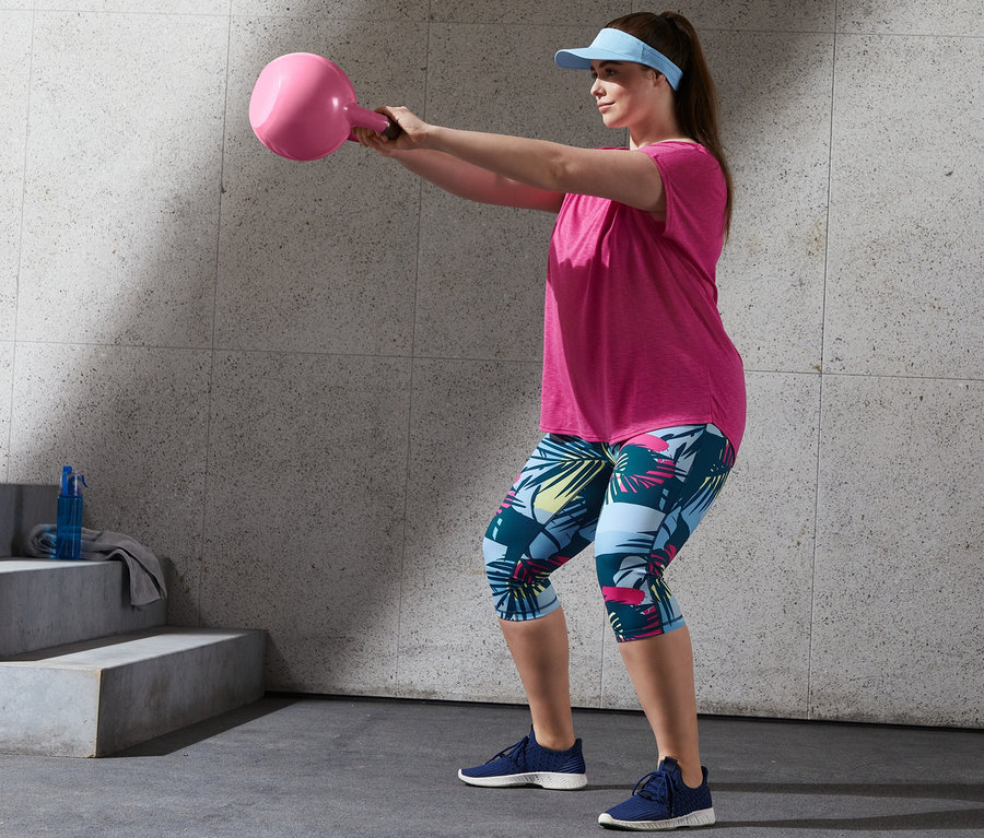Femme s'entraînant avec un T-shirt de sport rose vif et un corsaire de sport, tenant un kettlebell rose.