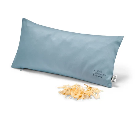 Un coussin bleu clair garni de copeaux de pin cembro, env. 40 x 20 cm, est posé sur un fond blanc à côté d'un tas de copeaux.