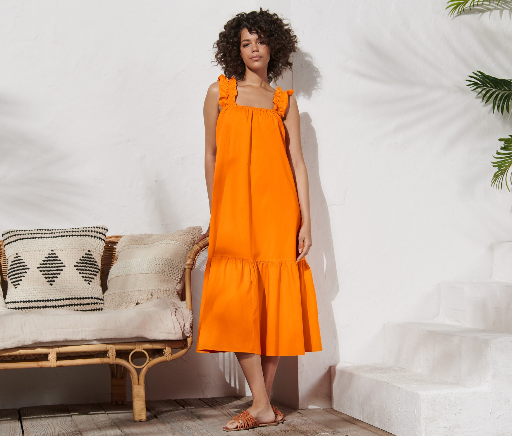 Une femme pose debout dans une robe en popeline orange.