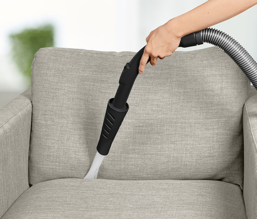 Une main nettoie un fauteuil en tissu avec un embout d'aspirateur.