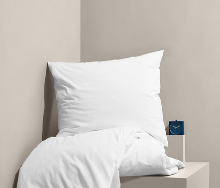 Linge de lit blanc en percale sur un lit à côté d'un réveil bleu.