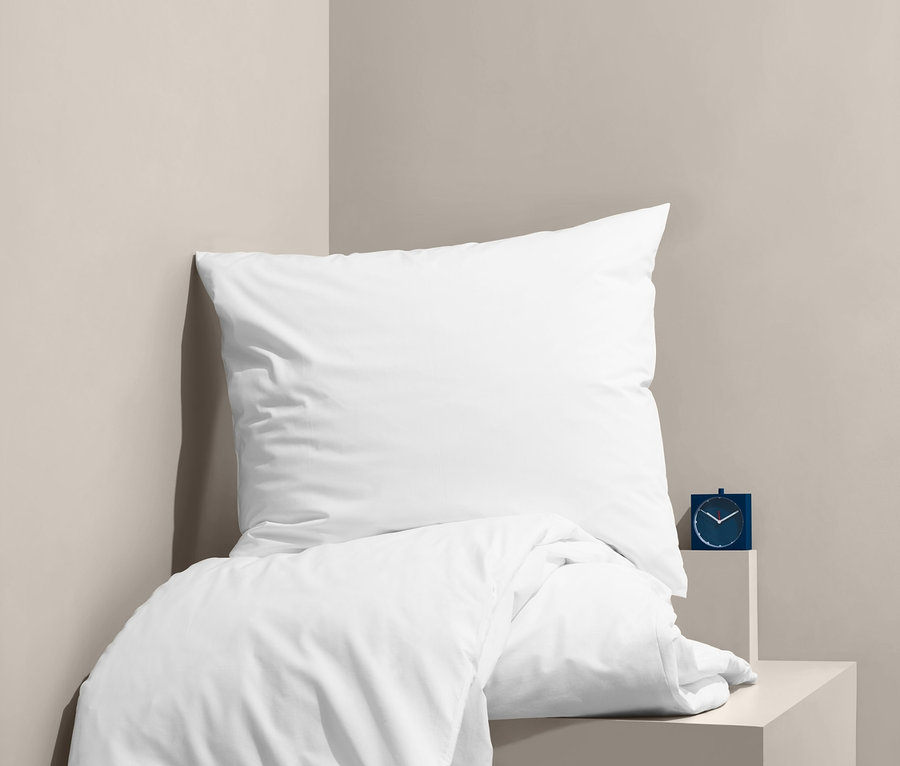 Linge de lit blanc en percale sur un lit à côté d'un réveil bleu.