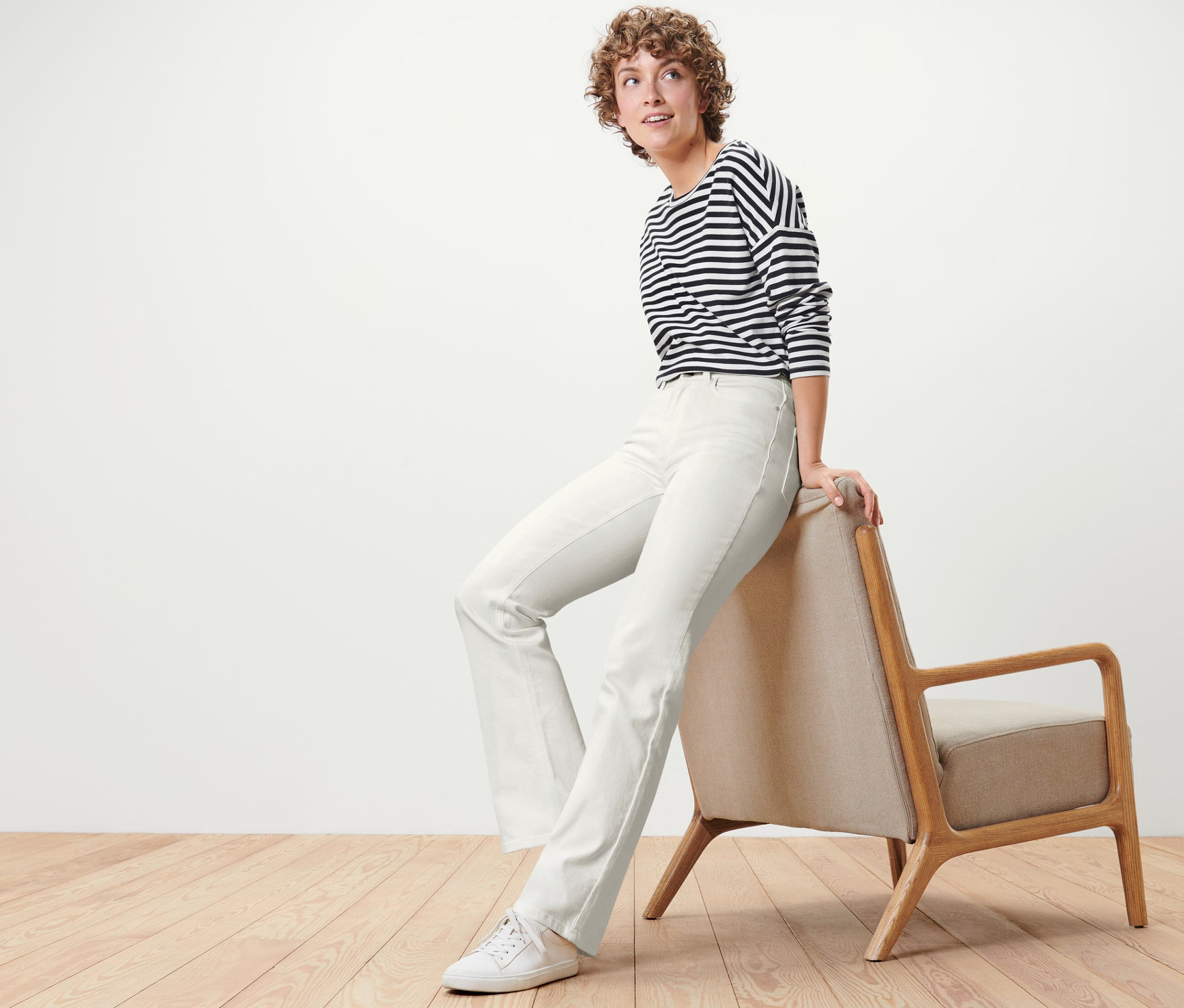 Une femme est assise sur un fauteuil et porte un jean bootcut blanc crème – Fit « Lou ».