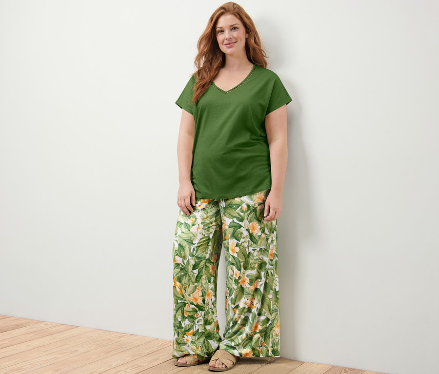 Une femme debout porte un haut vert avec empiècement au crochet et un pantalon palazzo imprimé.