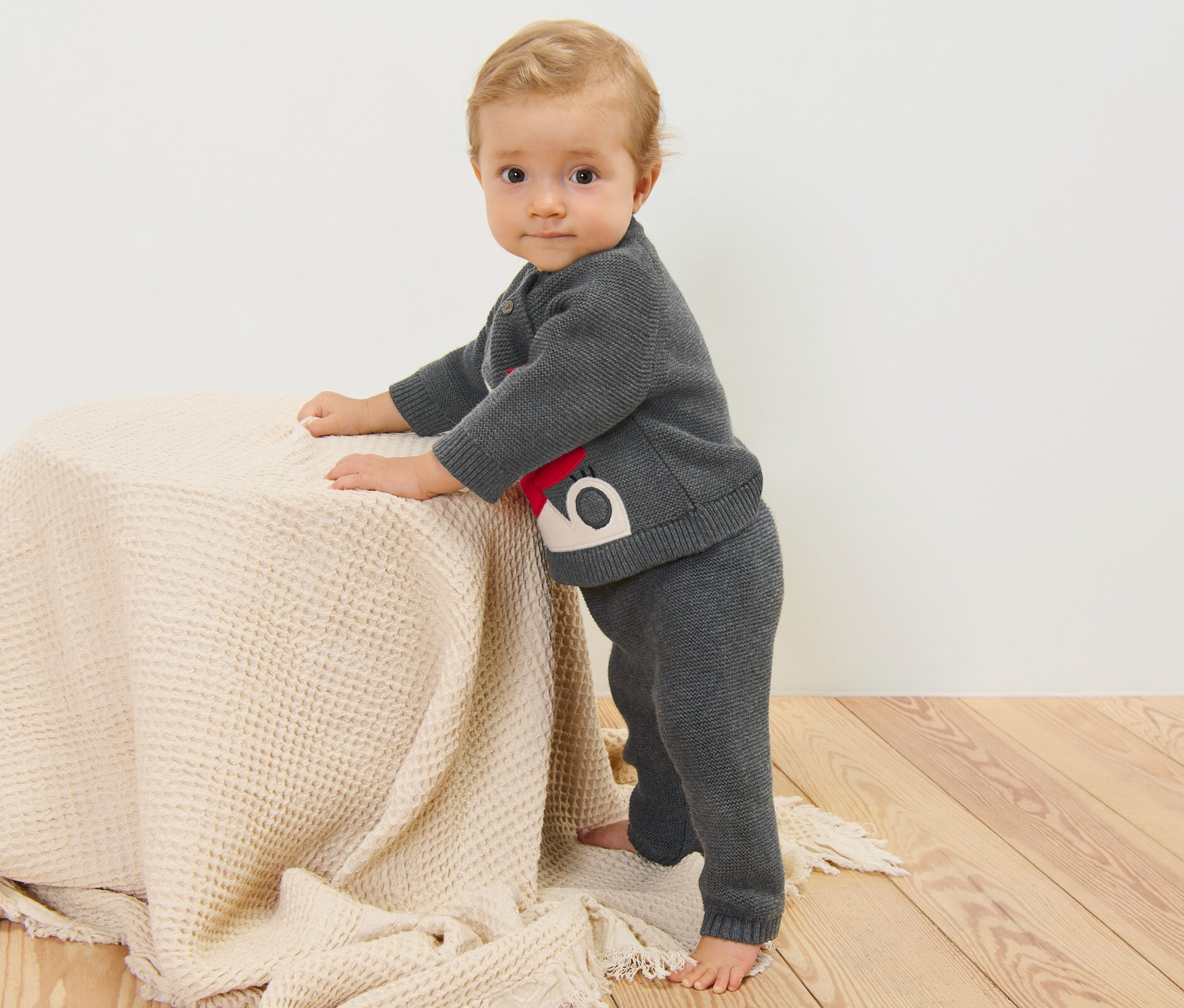 Un bébé debout s'appuie sur une table. Il porte un collant enfant.