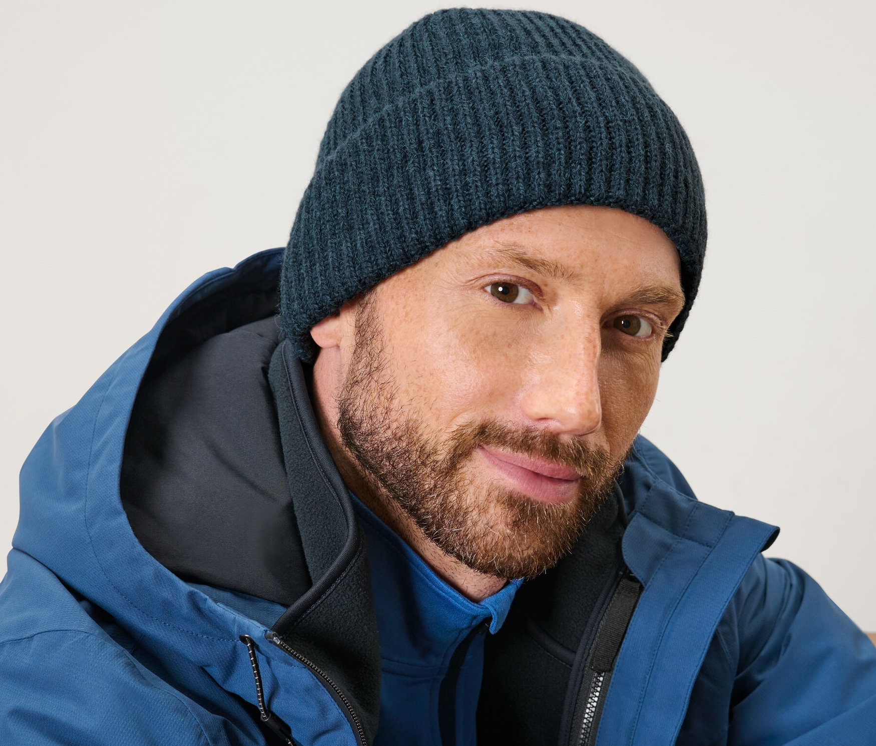 Un homme barbu porte un bonnet en maille bleu et une veste bleue.