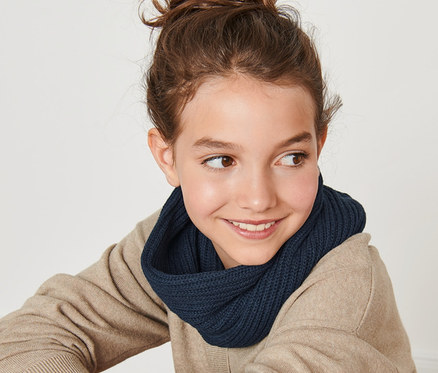 Une jeune fille souriante est assise dos à la caméra et porte une écharpe-tube en maille.