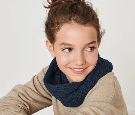 Une jeune fille souriante est assise dos à la caméra et porte une écharpe-tube en maille.