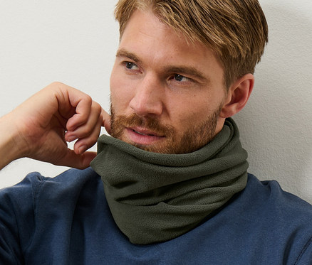 Un homme aux cheveux bruns et à la barbe porte un pull bleu et un col en polaire thermique.