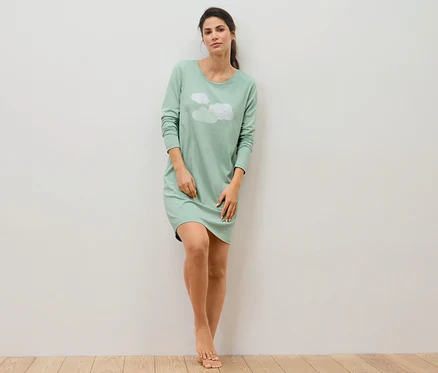 Femme appuyée contre un mur en chemise de nuit.