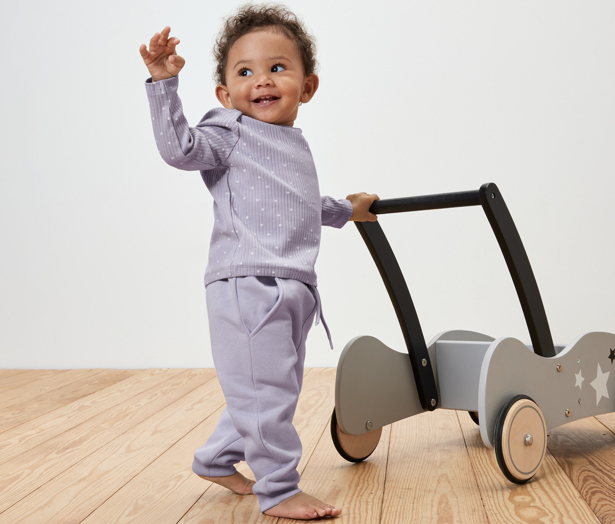 Un bébé pousse un trotteur et porte 2 pantalons en sweat pour bébé, à pois.