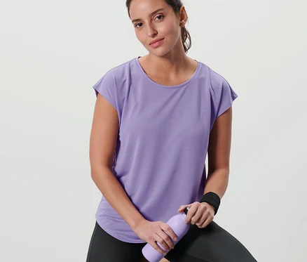 Femme assise sur un tabouret portant un t-shirt de sport lilas, tenant une bouteille violette.