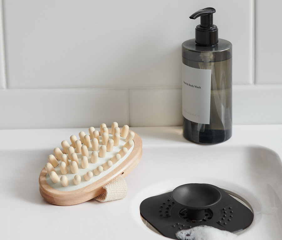Dans le lavabo, il y a un tamis / bonde d'écoulement, à côté se trouvent une brosse de massage et un flacon de savon.