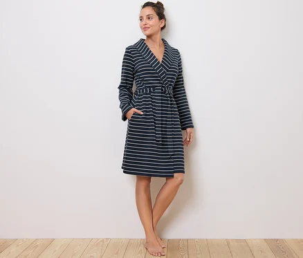 Une femme debout porte une robe de chambre rayée.