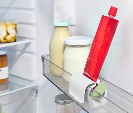Un tube rouge est placé dans un presse-tube avec clip pour réfrigérateur sur l'étagère du réfrigérateur à côté d'autres aliments.