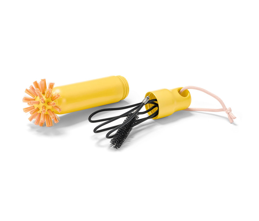Une brosse de vidange 2 en 1 jaune avec des poils orange est posée à côté d'un boîtier avec des brosses de nettoyage noires.