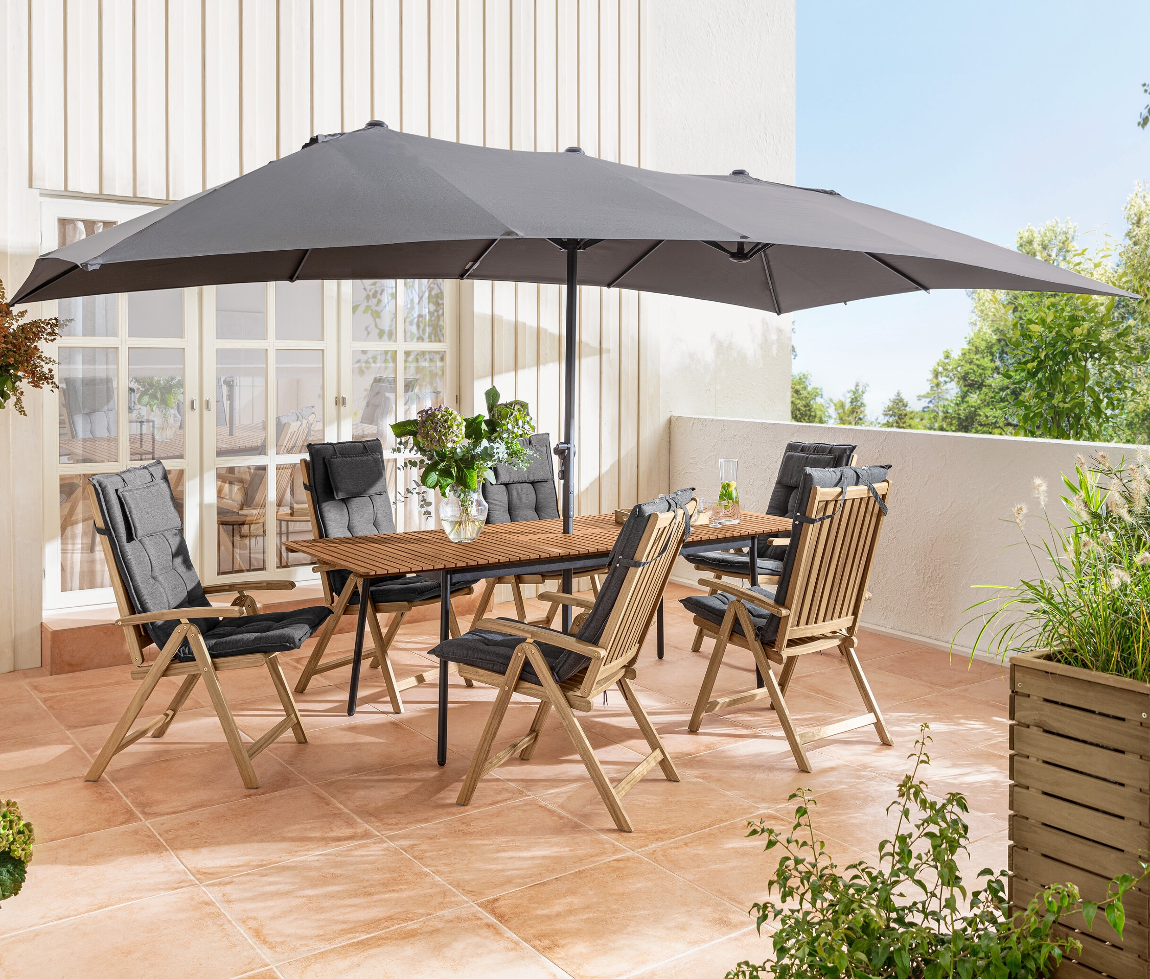 Terrasse avec table à rallonge «	Elin	» et chaises en bois «	Lenja	» avec housses Sun Garden sous un grand double parasol anthracite Leco.