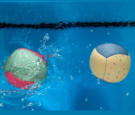Deux ballons de plage dans l'eau. L'un est vert avec des bords roses et l'autre est jaune avec des bords bleus.